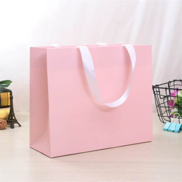 बाजूच्या कोनातून सानुकूल गुलाबी गिफ्ट पेपर बॅग प्रदर्शित करा