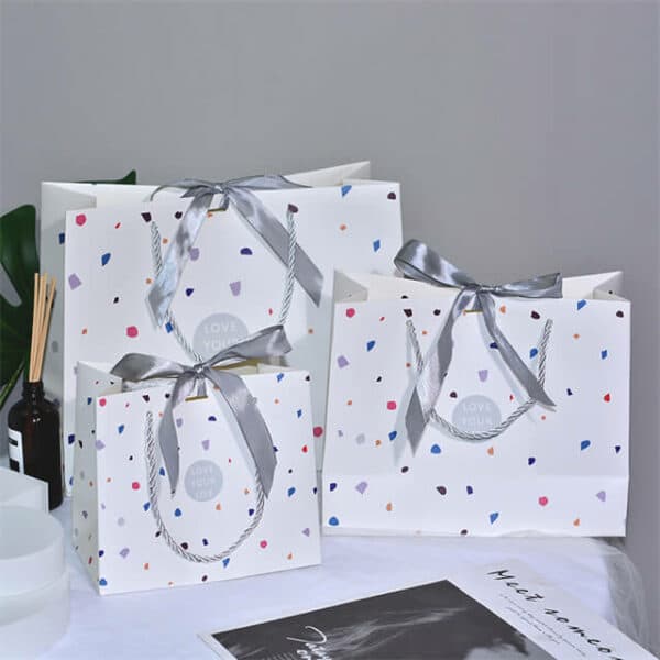 Parādiet trīs pielāgotus krāsainus dāvanu papīra maisiņus ar dažādu izmēru lentes banti