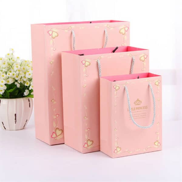 Exhiba tres bolsas de papel de regalo laminadas mate personalizadas de color rosa en diferentes tamaños