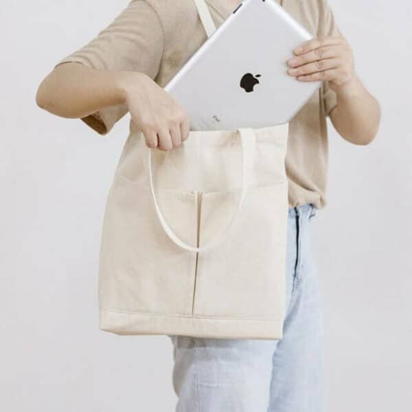 A person is packing the iPad into the canvas bag on his shoulder