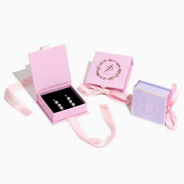 три прилагодени кутии за накит со панделки, од кои две се розови и една виолетова.