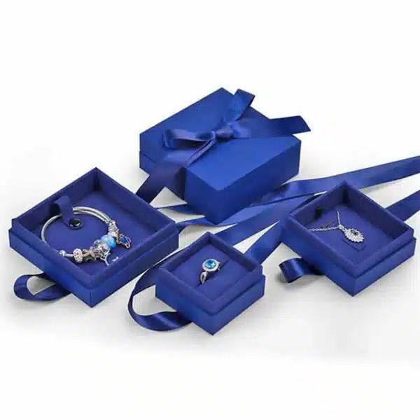 demonstruokite keturias pasirinktines tamsiai mėlynos spalvos papuošalų dėžutes su kaspinu ir papuošalais viduje