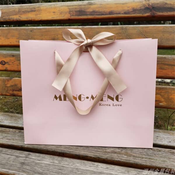 покажите один розовый нестандартный однотонный подарочный бумажный пакет с ленточным бантом на деревянной скамейке