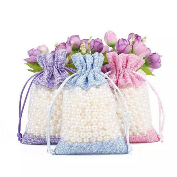 Trys skirtingų spalvų individualūs džiuto dovanų maišeliai, pilni perlų viduje