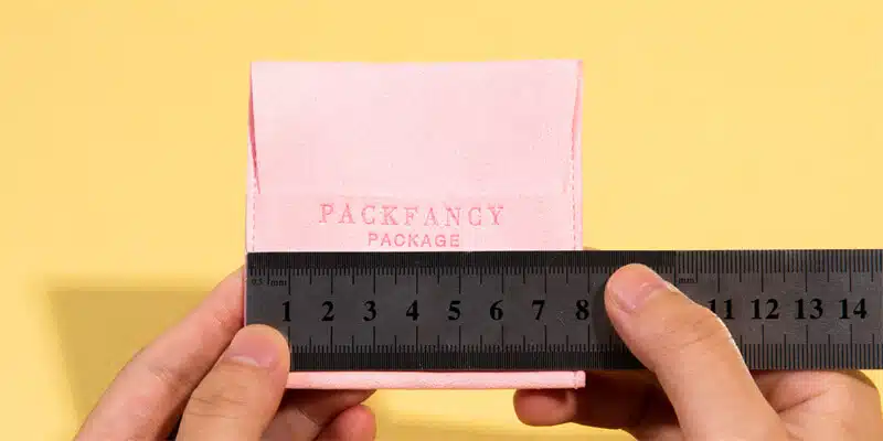 two hands holding a ruler to measure the dimensions of a pink jewelry pouch