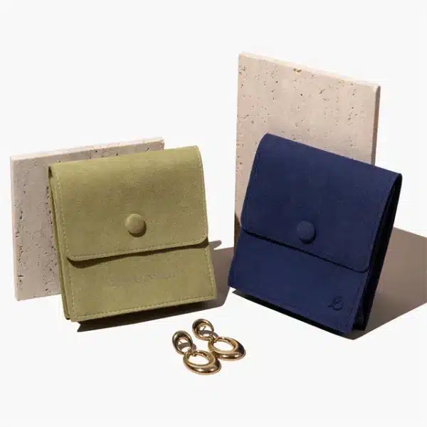 маслинесто зелена и сина прилагодена торбичка за накит со затворачи со копчиња, одделно стои на две беж шкрилци, со пар златни обетки пред нив.