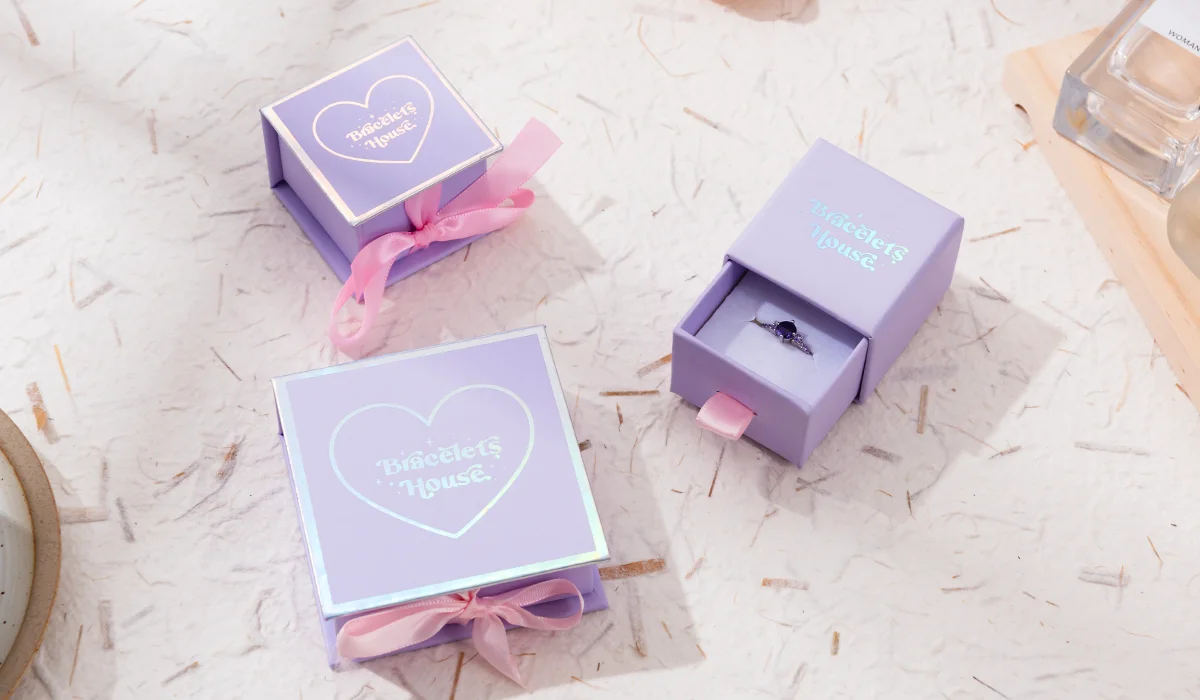 ელეგანტური იასამნისფერი საბაჟო ბრენდის სასაჩუქრე ყუთები ჰოლოგრაფიული ფოლგის ბეჭდვით, ერთი ღია ყუთი ბეჭდის გამოსახულებით, ტექსტურირებული თეთრ ფონზე.