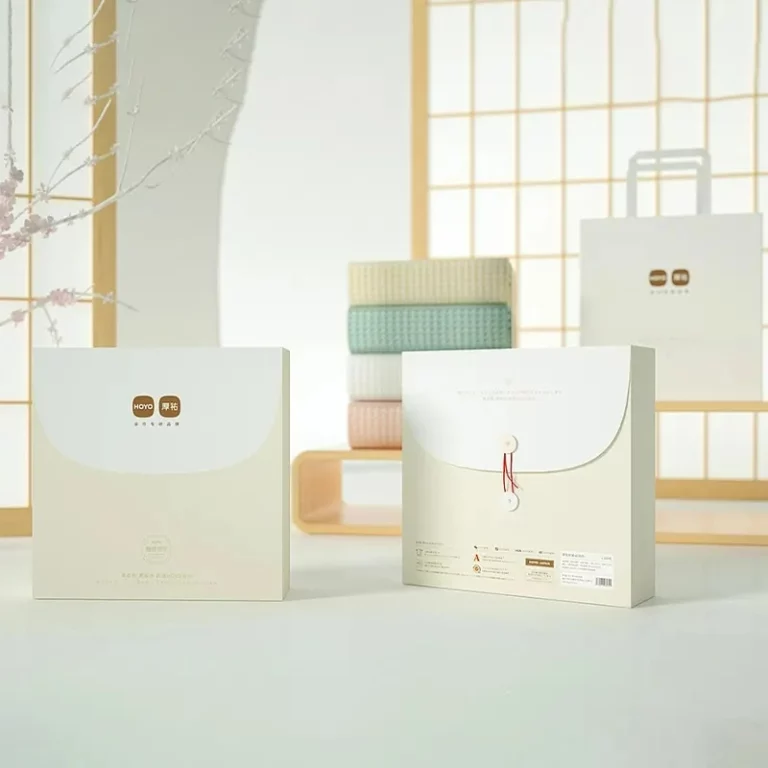 ორი ელეგანტური პირსახოცის შესაფუთი ყუთი მინიმალისტური დიზაინით, ერთი წითელი სიმებით დახურული, მშვიდ ფონზე, რბილი განათებით და იაპონური სტილის დეკორით.