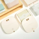 რბილი პასტელის ფერის პირსახოცების ელეგანტური შეფუთვა, გამოფენილი ღია და დახურულ ბიოდეგრადირებად ყუთებში ხის თაროზე.