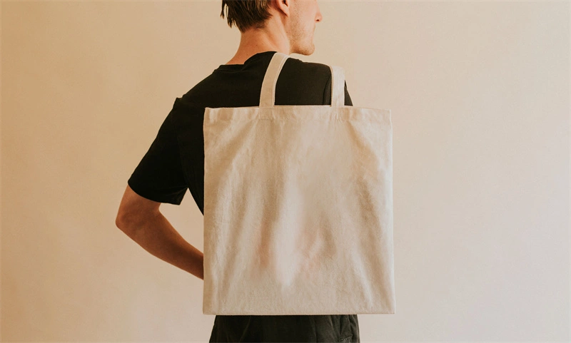 Was ist eine Seitenfaltentasche? Blog-Illustration: Eine Person trägt ein schwarzes Hemd und eine große beige Einkaufstasche über der Schulter.