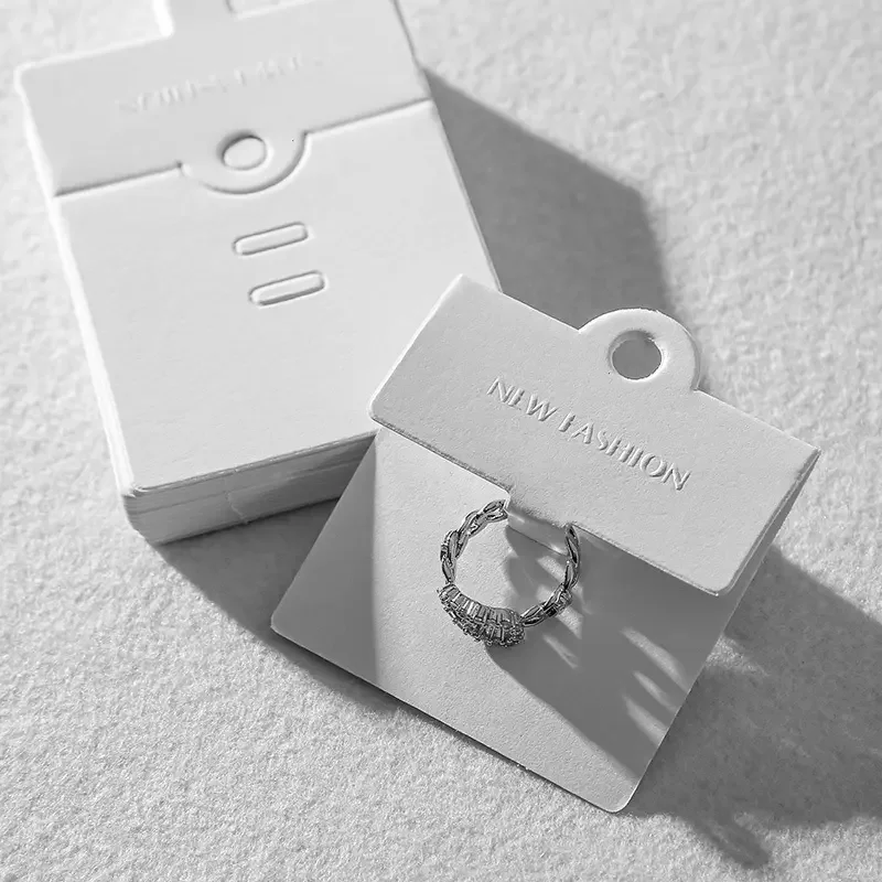 Weiße Schmuckpräsentationskarten mit der Aufschrift „NEW FASHION“ und einem silbernen Ring.