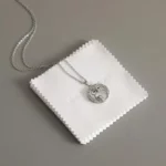 Eine silberne Eulenkette auf einem Stapel weißer Schmuckpoliertücher mit der Aufschrift „Beste Wünsche für Sie“.