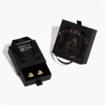 ორი შავი მორგებული ხისტი უჯრის სამკაულების ყუთი სახელურებით, ერთი ღიაა საყურეებით შიგნით, მეორე დგას მის მარჯვნივ