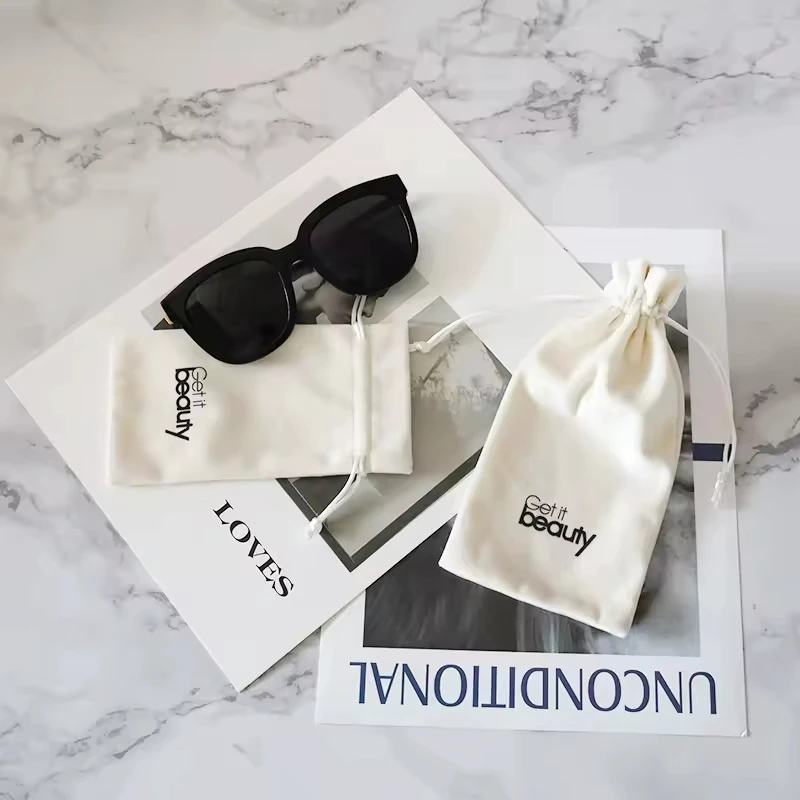 შავი სათვალე, რომელიც განთავსებულია ჟურნალის თავზე, ორი თეთრი ქსოვილის გასამაგრებელი ჩანთებით, წარწერით "Get it Beauty". ფონი მარმარილოს ზედაპირია.