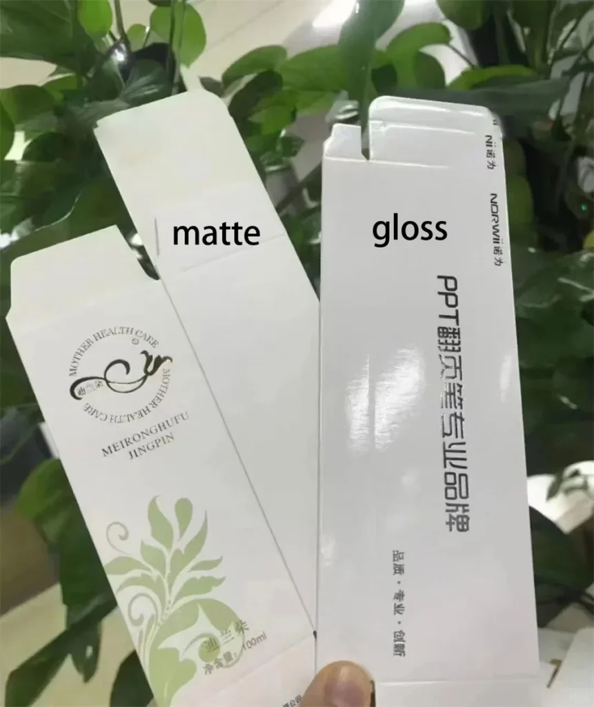Mattes vs. glänzendes Laminat: Welche Verpackungsoberfläche passt am besten zu Ihrer Marke? 6 Eine Hand hält zwei auseinanderklappbare Kartons mit matter und glänzender Laminierung separat.